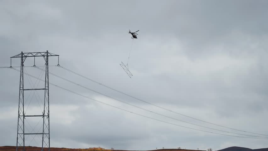 A cargo helicopter with a lifting cable and load attached makes a delivery in the difficult-to-reach mountainous terrain.
