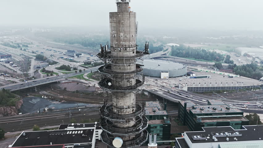 Aerial medium shot of a bleak industrial concrete television and radio link tower in Pasila, Helsinki, Finland on a bright and foggy day. Camera orbiting around, Arena and railways in background. Royalty-Free Stock Footage #1110637285