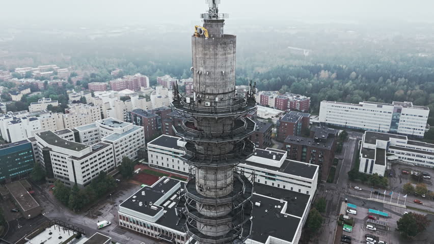 Aerial shot of a bleak industrial concrete television and radio link tower in Pasila, Helsinki, Finland on a bright and foggy day. Camera orbiting around, apartment buildings and forest in background. Royalty-Free Stock Footage #1110637287