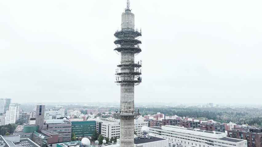 Aerial approaching low angle shot of a bleak industrial concrete television and radio link tower in Pasila, Helsinki, Finland on a bright and foggy day. Sky and apartment buildings in background.