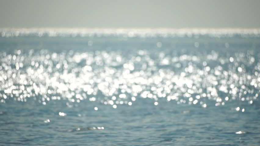 Blurred golden sea at sunset. The sun reflects and sparkles on the waves with bokeh, illuminating the golden sea. Holiday recreation concept. Abstract nautical summer ocean sunset nature background.