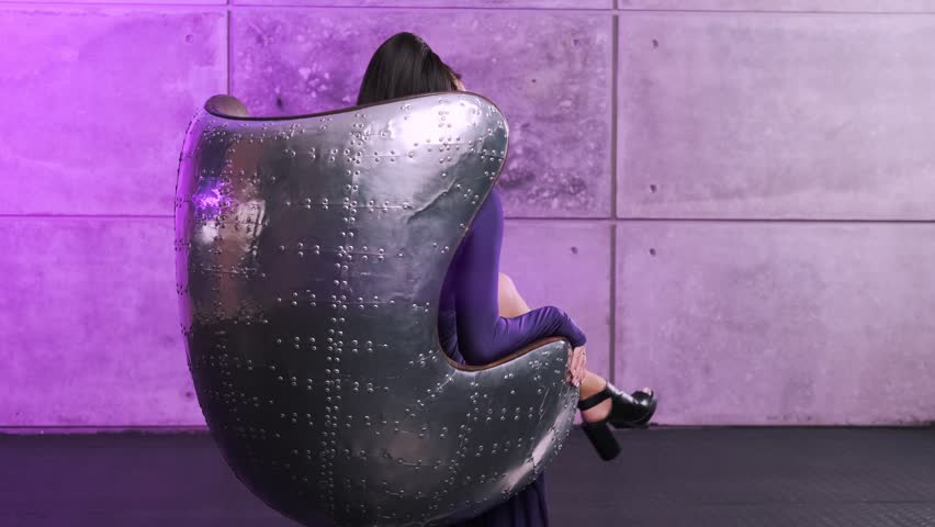 Beautiful go-go girl in a purple dress with rhinestones poses on a metal chair. Turns around in his chair and looks at the camera. Party concept, night club
