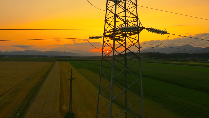 AERIAL: Flying up the high voltage electricity tower and power lines at sunset above the beautiful agricultural field Royalty-Free Stock Footage #11106425