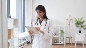 Portrait of friendly female physician in lab coat holding digital tablet and looking proudly at camera. Indian woman working in hospital using modern gadgets. Concept of perfect medical service. - Powered by Shutterstock - Get 15% off with code: PIKWIZARD15