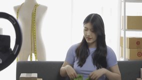 Asian girl selling clothes online using laptop at apartment, fashion blogger records video for online blog, cute woman in live broadcast on internet clothing store at home