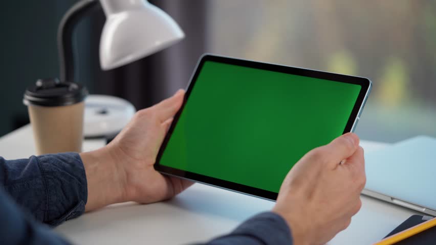 Young Man Using Tablet Computer with Green Screen Mock Up Display. Male Watching Videos and Reading Social Media Posts on Mobile Device. Close Up of Tablet in Man's Hands - Powered by Shutterstock - Get 15% off with code: PIKWIZARD15