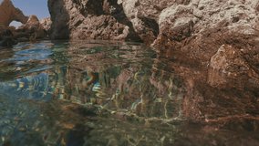 POV shot, guy paddling with his hands underwater swims along rocky shore. First person video, man swims on surface in shallow water of Mediterranean sea