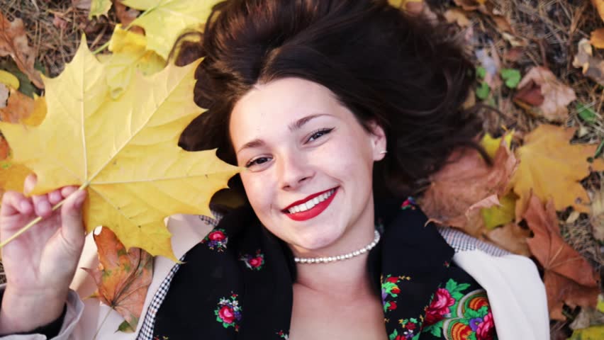 The girl lies on the yellow fallen leaves and leaves fall on her. Autumn concept.