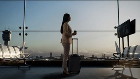 Side View Of Asian Businesswoman With Rolling Suitcase In Boarding Lounge Of Airline Hub, Drinking Coffee While Waiting For Flight, Airport Terminal With Airplane Takes Off Outside The Window - Powered by Shutterstock - Get 15% off with code: PIKWIZARD15