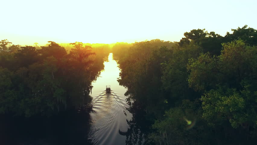 Aerial Forward Shot Of Boat On River Amidst Green Trees And Plants Against Sky At Sunset - Bayou, Louisiana