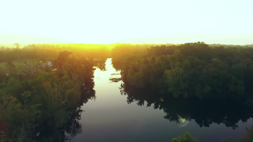 Aerial Ascending Forward Shot Of River Amidst Green Trees And Plants Against Sky At Sunset - Bayou, Louisiana