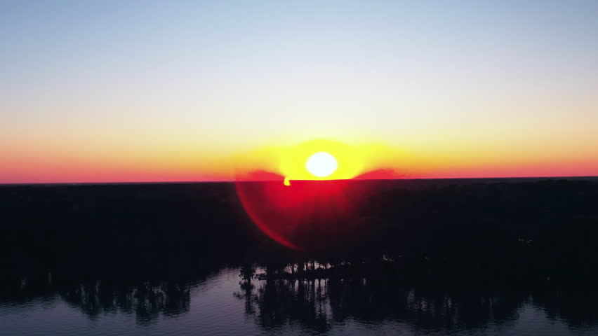 Aerial Backward Shot Of Sun Over Silhouette Landscape With River Against Sky At Sunset - Bayou, Louisiana