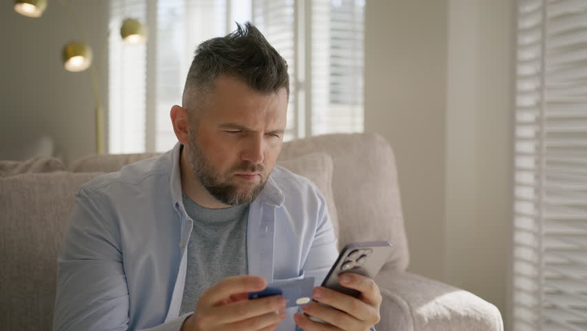 Upset guy feels angry due lack of money, insufficient funds fraud. Stressed mature gray haired man sit on sofa with smartphone and credit card in hands, frowns and sighs try to make internet purchase Royalty-Free Stock Footage #1110674513