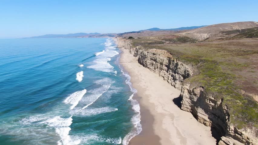 Aerial video shoot of Pescadero Coast shore that goes all over the horizon, along with the sea on the left and cars by the road in San Mateo, California.
