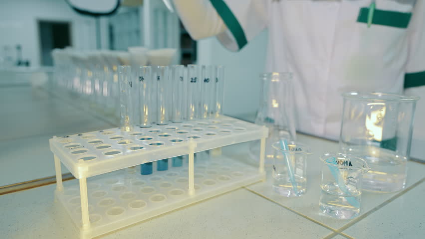 Laboratory technician pours white liquid into test tubes and checks the reaction, fake medicine. Adding the reagent to the test tubes, conducting the experiment in the laboratory. Close up.