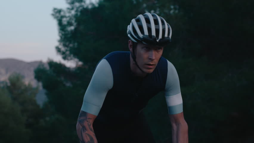 Fit and concentrated male cyclist on heavy cardio training. Young professional athlete climb up mountain hill on carbon road bike. Cinematic cycling during evening training session Royalty-Free Stock Footage #1110684267