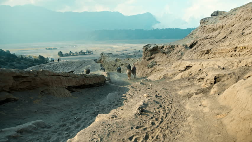 An Indonesian man with a dark brown horse rides people in the middle of the desert.