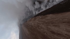 Vertical video. FPV drone dive down from active volcanic crater summit natural gas stream danger heat extreme. Aerial dynamic speed view eruption volcano smoke falling stones lava disaster explosion