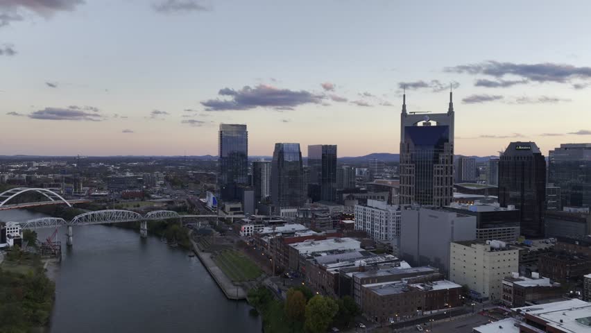 Aerial drone footage of downtown Nashville skyscrapers during a beautiful pink and purple sky sunset. Video taken in late October with colorful trees lining the Cumberland River. Royalty-Free Stock Footage #1110685491