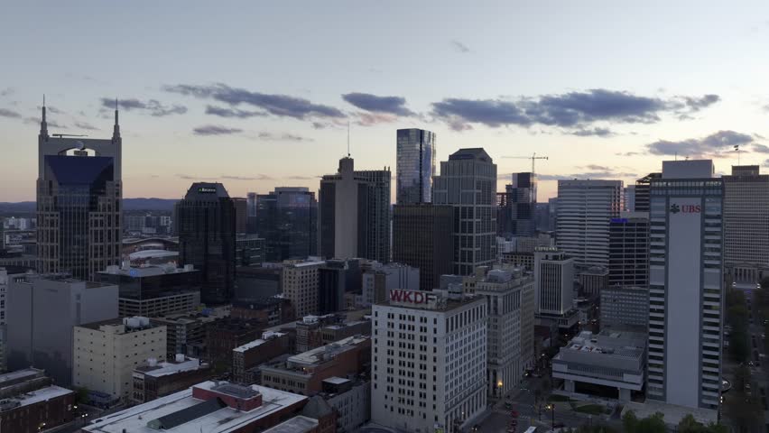 Aerial drone footage of downtown Nashville skyscrapers during a beautiful pink and purple sky sunset. Video taken in late October with colorful trees lining the Cumberland River. Royalty-Free Stock Footage #1110685493