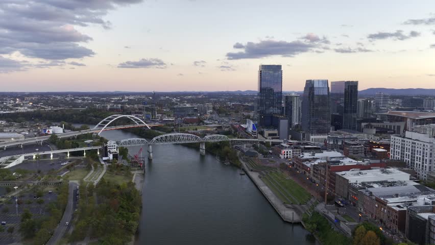 Aerial drone footage of downtown Nashville skyscrapers during a beautiful pink and purple sky sunset. Video taken in late October with colorful trees lining the Cumberland River. Royalty-Free Stock Footage #1110685507