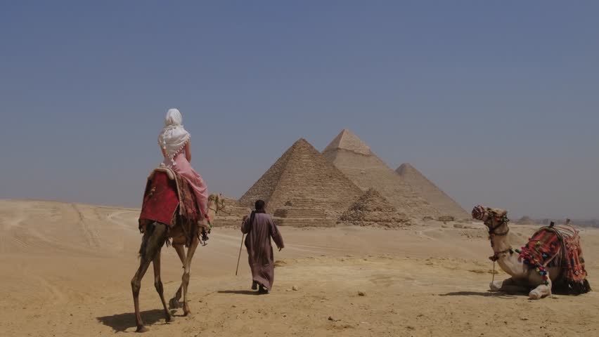 Young woman sits atop a camel in Egypt. Great Pyramids of Giza.