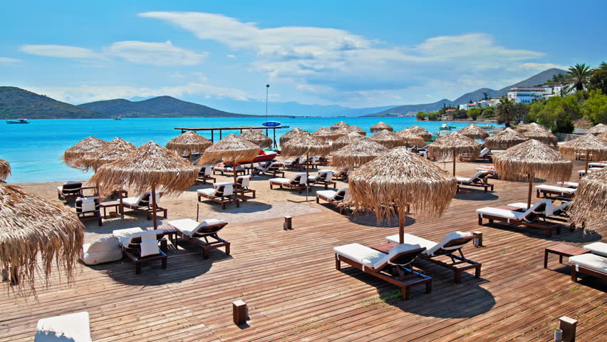 Beautiful beach with blue crystal water with boats on the Mediterranean Sea. The coastal Greek island of Crete with turquoise water and beach parasols on the seashore.