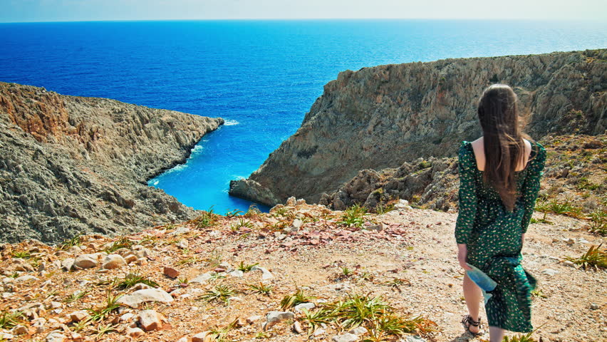 A beautiful girl looking at the sandy beach in a cove surrounded by rock formations at Seitan Limania, Crete. A young woman enjoying the picturesque panoramic views with a stunning crystal blue beach.