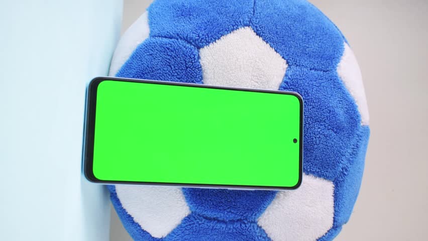 Vertical video of hand taking smartphone with green screen next to soccer ball Royalty-Free Stock Footage #1110690403