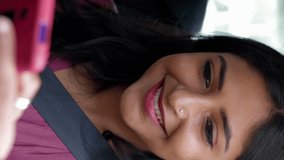 Happy young indian woman using cell phone sitting in the back seat of a car. Technology and transport concept. Vertical aspect video 9:16