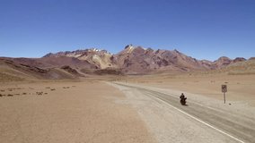 side view man on motorcycle followed by drone discovering a lonely desert road with mountains and lagoons 