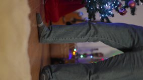 Vertical video, close-up of the legs of a dancing man near a Christmas tree