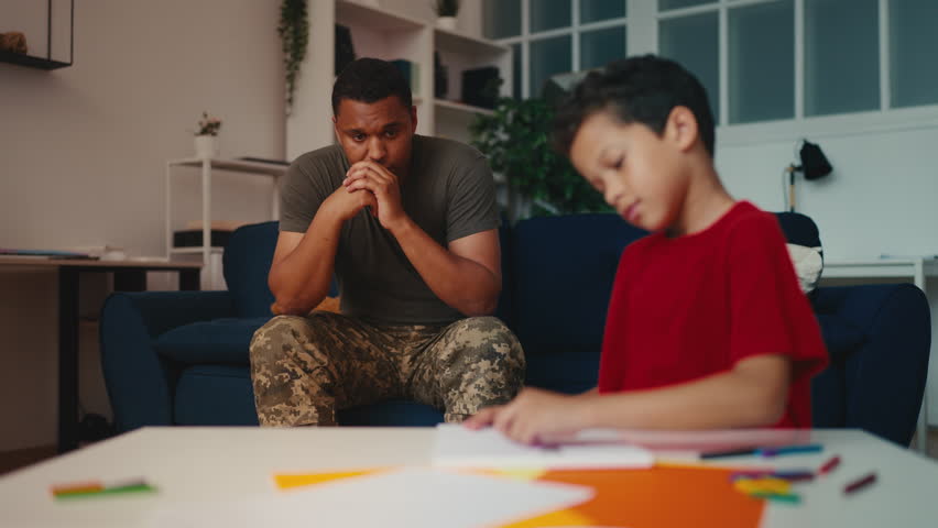 Upset military man looking at little kid drawing picture, leaving home for war