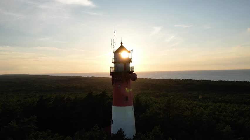 Lighthouse tower at sunset, cinematic aerial view. Silhouette view of beautiful lighthouse at sea shore, on the top of forested hill, Baltic sea. | Shutterstock HD Video #1110710643
