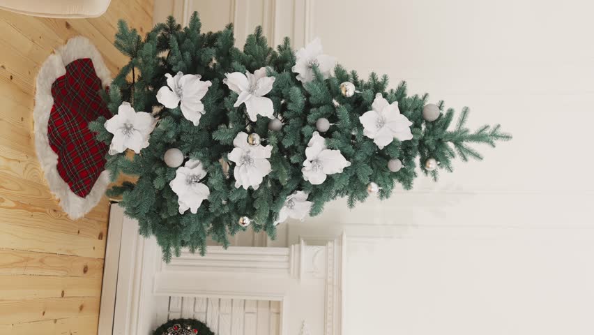 a girl in a red sfetra approaches a decorative Christmas tree and clings to garlands of large white flowers. vertical video