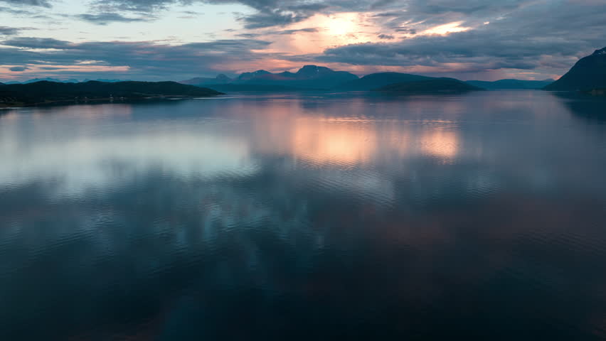 Colourful sunset and reflection in Norwegian fjord. Mountain backdrop, drone time lapse.