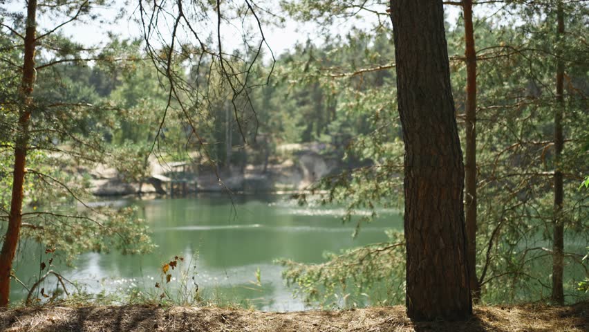 Woman hiker walking trail around mountain lake at sunny morning in autumn pine forest at warm day. female traveler with yellow backpack hiking in woods, adventure outdoor lifestyle.