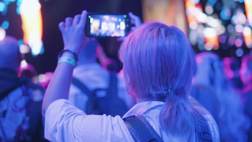 Girl takes video on phone at music anime cosplay gaming convention concert.