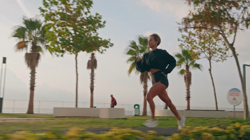 Tracking shot of Young fitness sports woman running outdoors on the promenade during sunset. High quality 4k footage