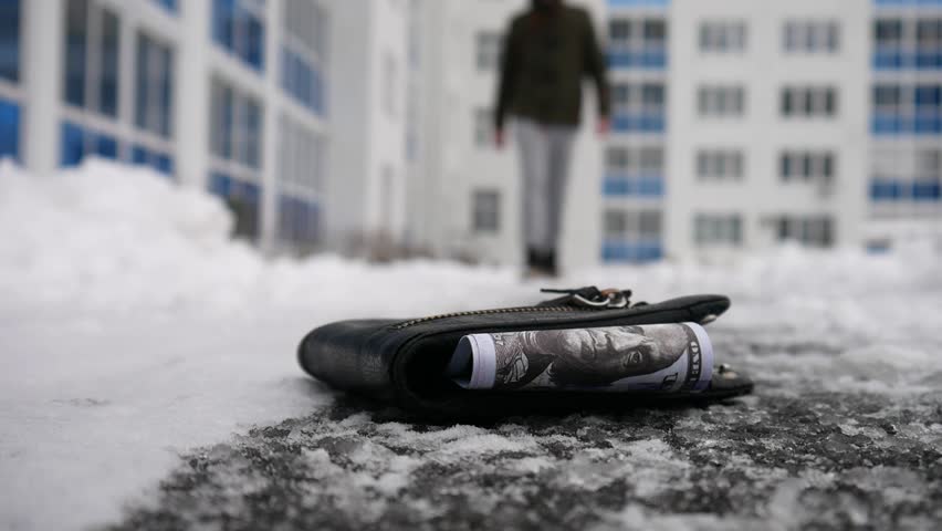 A lost wallet on the snowing path with hundred dollar bills in it close-up and a random man picks it up