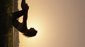 Woman breathing in fresh morning air at sunrise near lake, introducing and performing yoga for harmony and relaxation of body and spirit. Vertical video woman performing asana, tuning in to new day.