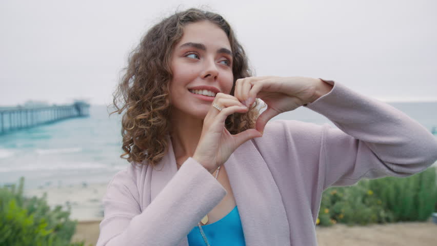 Love, thank you, grateful, support, good deed volunteer concept. Close up portrait 20s european woman show heart sign make symbol with hands. Cute girl feels grateful smiling looks at camera at ocean - Powered by Shutterstock - Get 15% off with code: PIKWIZARD15