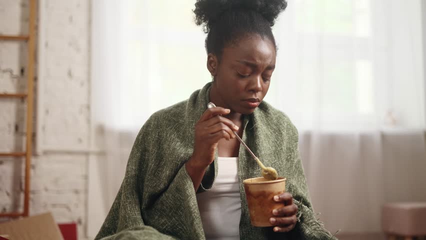 Portrait of sad young woman dealing with stress by eating food sitting on bed at home Upset brunette female wrapped in blanket crying and eating ice cream indoors alone Mental heath problem Royalty-Free Stock Footage #1110732803