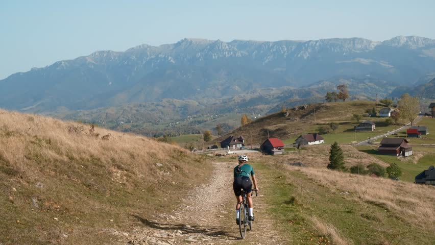 Woman cyclist riding gravel bicycle in mountains.Gravel cycling.Biking adventures.Cycling in nature on sunny summer day. Female riding in beautiful landscape.Healthy lifestyle. Cyclist twisting pedals