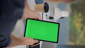 Young Man Using Tablet Computer with Green Screen Mock Up Display. Male Watching Videos and Reading Social Media Posts on Mobile Device. Close Up of Tablet in Man's Hands