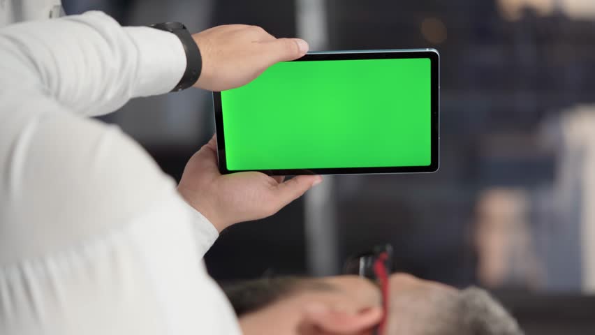 Bearded Man in Glasses Using Tablet Computer with Green Screen Mock Up Display. Male Watching Videos and Reading Social Media Posts on Mobile Device. Shooting Close Up Over the Shoulder