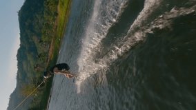 Vertical video 4k. Wakeboarder man ride touch water hand cable wakeboard park in lake. Sport extreme activity athlete guy doing simple trick springboard backflip training practicing cable wakeboarding