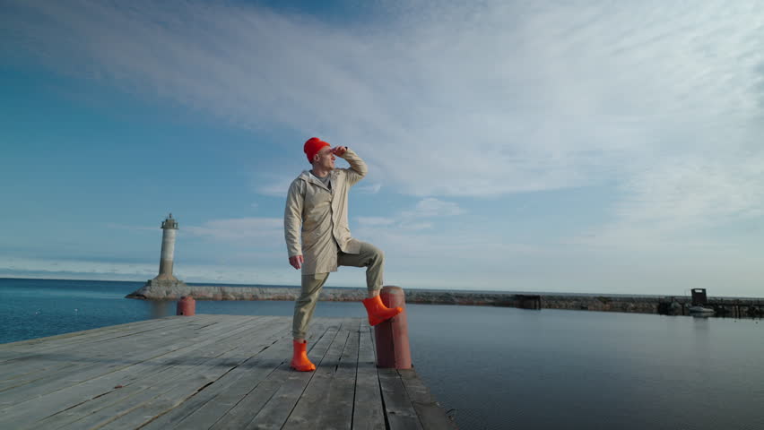 Traveler Or Sailor Standing Alone On Old Wooden Pier In Bay Near Lighthouse And Looking Far