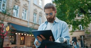 Portrait of calm young confident freelance employee working outdoors. Male businessman concentrate at work, holding digital tablet, looking at screen. Freelance online work, internet, modern devices.