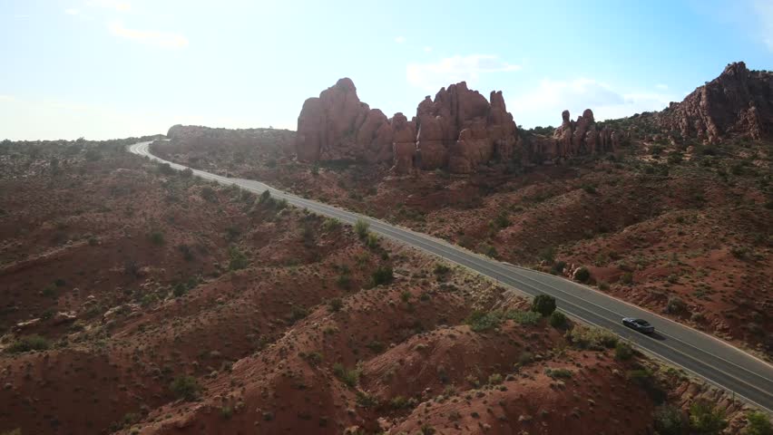 An expansive drone shot capturing the panoramic beauty of Arches National Park, featuring a winding road with an unidentifiable car traveling along it.
